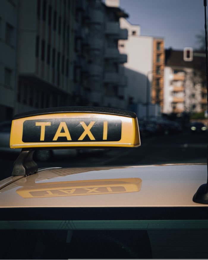contact-img Close-up of a taxi sign on a car roof with an urban city background.