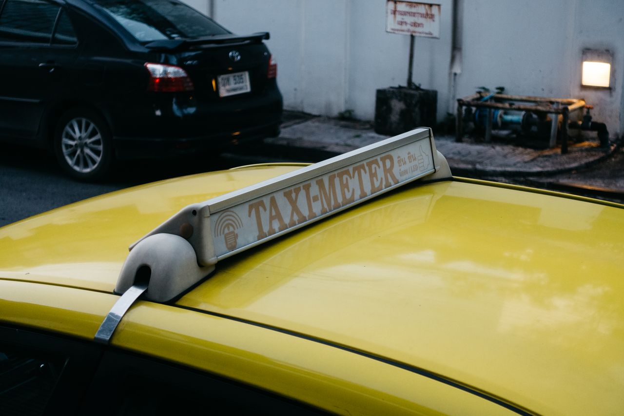 our-experience Close-up of a yellow taxi's roof with a taxi meter sign in an urban environment.